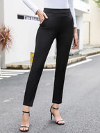 Femme portant un pantalon noir ajusté et un haut blanc à manches longues, debout sur une rue pavée. Mode élégante, tenue chic, talons hauts.