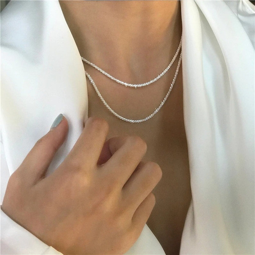 Collier double rangée en argent sur chemisier blanc, main féminine élégante, bijou moderne et chic, mode tendance, accessoire de luxe.