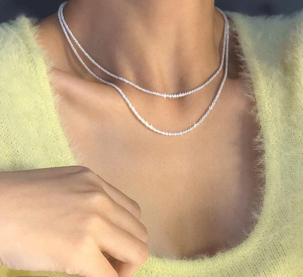 Collier double rang en argent sur un pull jaune doux, bijou élégant et tendance, accessoire mode femme, style chic et moderne.