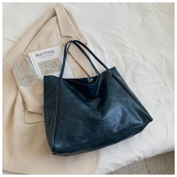 Sac à main en cuir noir sur un manteau beige, avec un verre transparent et un livre d'art Matisse. Accessoire mode élégant et tendance.