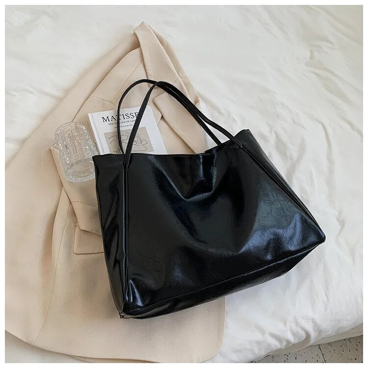 Sac à main noir en cuir brillant sur un manteau beige, avec un livre et une bouteille d'eau transparente. Accessoire mode élégant et tendance.