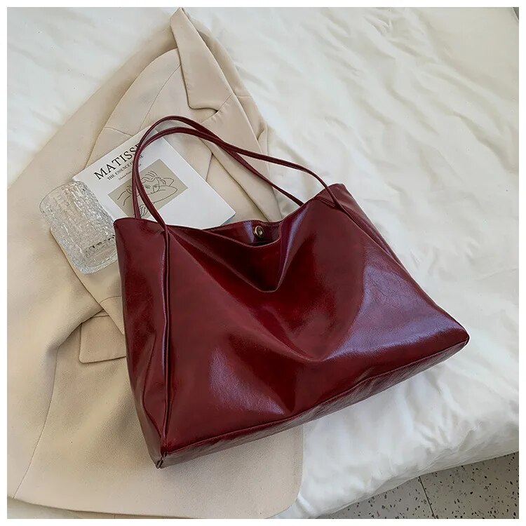 Sac à main en cuir rouge sur un manteau beige, posé sur un lit blanc. Accessoire élégant, mode féminine, style chic et moderne.