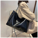 Femme assise avec un grand sac à main noir en cuir, élégant et moderne, sur une chaise transparente. Mode féminine, accessoires tendance.