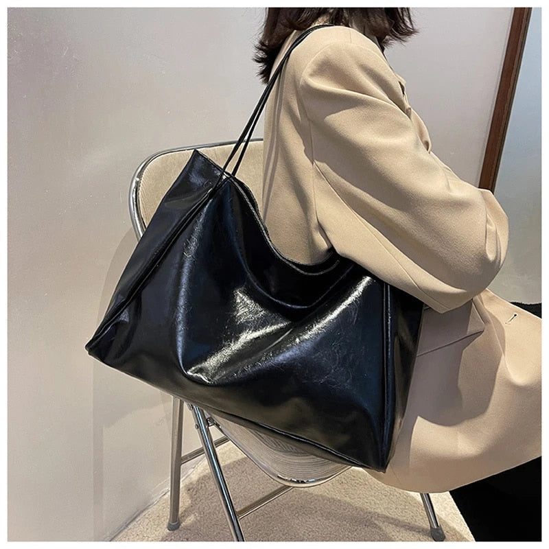 Femme assise avec un grand sac à main noir en cuir, élégant et moderne, sur une chaise transparente. Mode féminine, accessoires tendance.