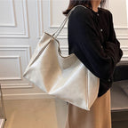Sac à main en cuir beige porté par une femme en pull noir et jupe marron, devant un mur blanc élégant. Accessoire mode chic et tendance.