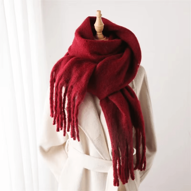 Écharpe rouge en laine épaisse avec franges, posée sur un mannequin en bois, idéale pour l'hiver. Accessoire mode chaud et élégant.