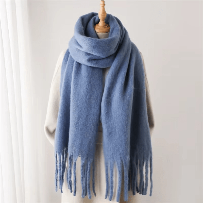 Écharpe en laine bleue avec franges, posée sur un mannequin, fond blanc. Accessoire mode hiver, chaud et élégant, tendance et confortable.