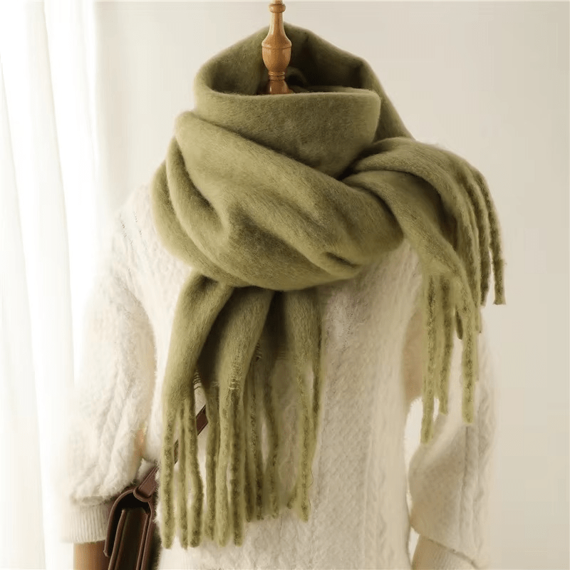 Écharpe en laine verte épaisse et douce, drapée sur un mannequin en pull blanc, avec franges élégantes. Accessoire hiver tendance et chaud.