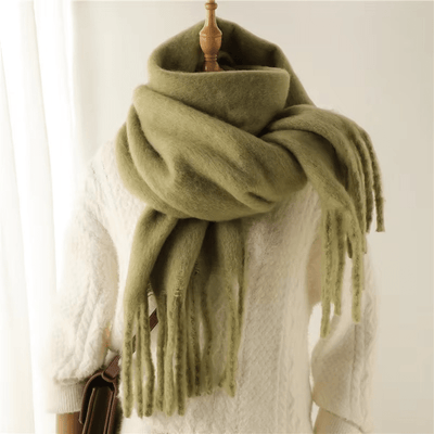 Écharpe en laine verte épaisse et douce, drapée sur un mannequin en pull blanc, avec franges élégantes. Accessoire hiver tendance et chaud.