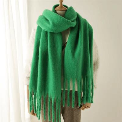 Écharpe verte en laine épaisse sur mannequin, franges longues, style hiver, accessoire mode chaud, tendance, confort, élégance, intérieur lumineux.