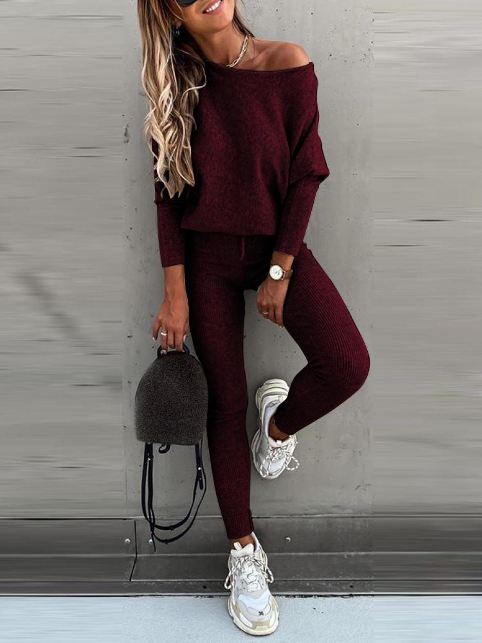 Femme en tenue décontractée bordeaux, pull ample et leggings, portant des baskets blanches et un sac à dos gris. Mode automne chic et confortable.
