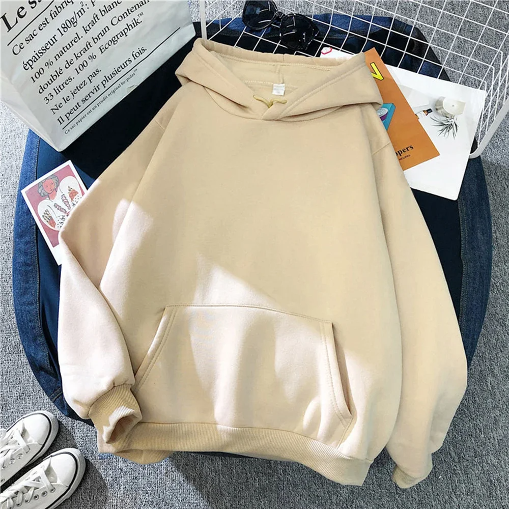 Sweat à capuche beige unisexe posé sur un fond gris, avec des accessoires comme des lunettes de soleil et des livres. Mode décontractée, tendance automne.