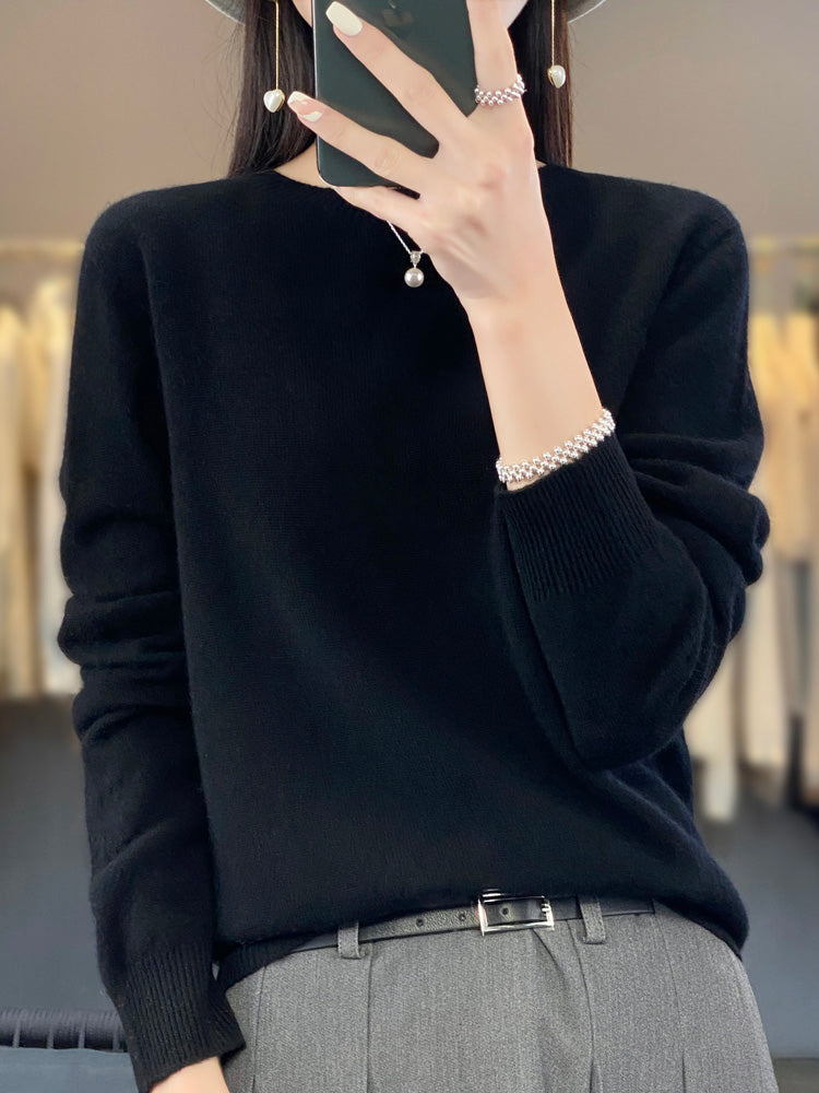 Femme en pull noir élégant, tenant un smartphone, portant un bracelet perlé et un pantalon gris. Mode automne, style chic et minimaliste.