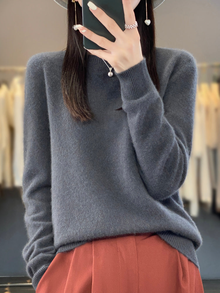 Femme portant un pull en cachemire gris, tenant un smartphone, avec un pantalon orange. Mode automne-hiver, style élégant et décontracté.