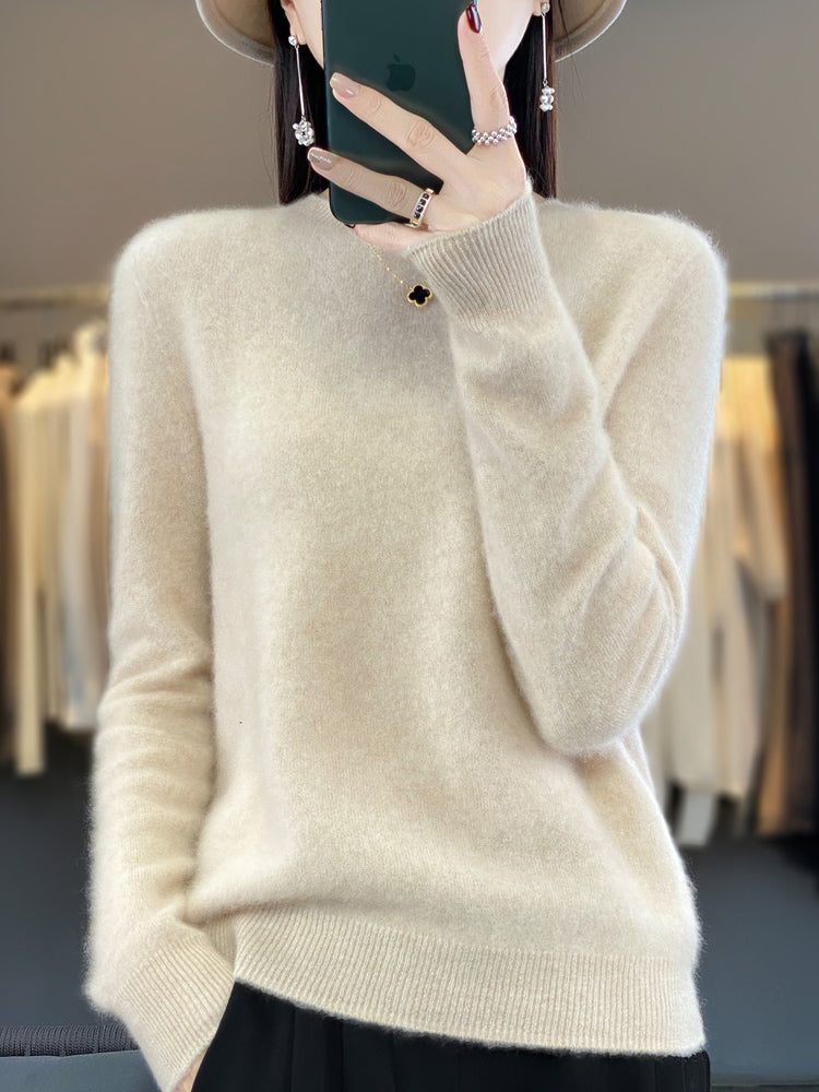 Femme portant un pull en cachemire beige, tenant un smartphone, avec des vêtements flous en arrière-plan. Mode automne-hiver, élégance décontractée.