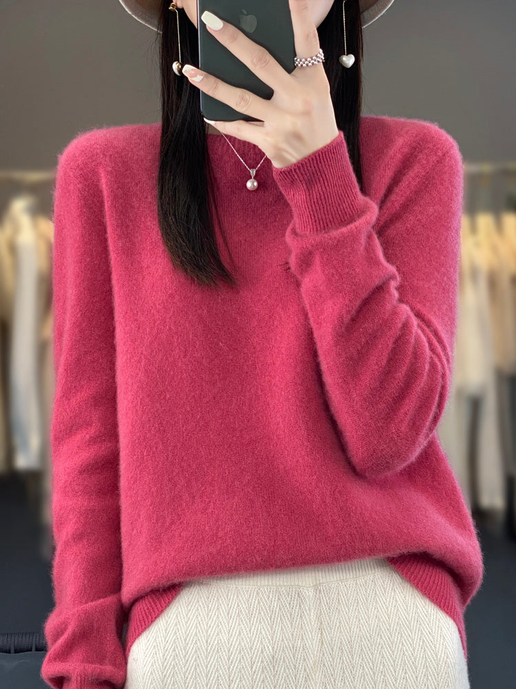 Femme portant un pull en cachemire rose, tenant un smartphone, avec un collier perle. Mode automne-hiver, style élégant et décontracté.