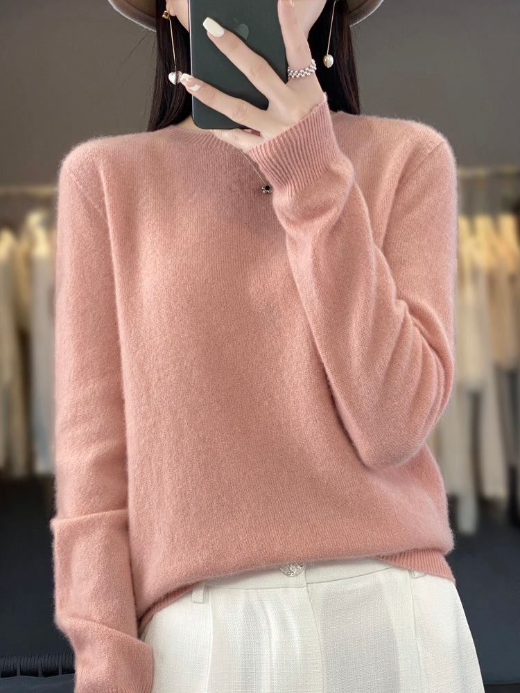 Femme portant un pull en cachemire rose doux, tenant un smartphone, avec un fond de vêtements flous. Mode automne-hiver, élégance décontractée.