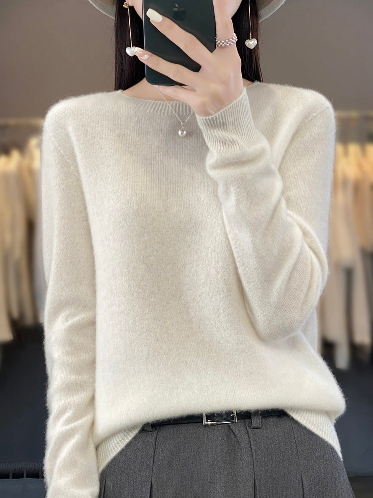 Femme portant un pull en cachemire blanc, accessoirisé d'un collier perle et d'un chapeau, devant un fond de vêtements flous. Mode élégante et chic.