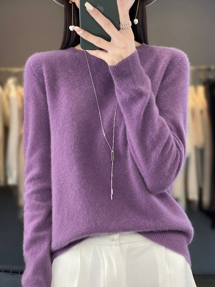 Femme portant un pull en cachemire violet avec un collier long, tenant un smartphone. Mode élégante, tenue automne-hiver, style décontracté chic.