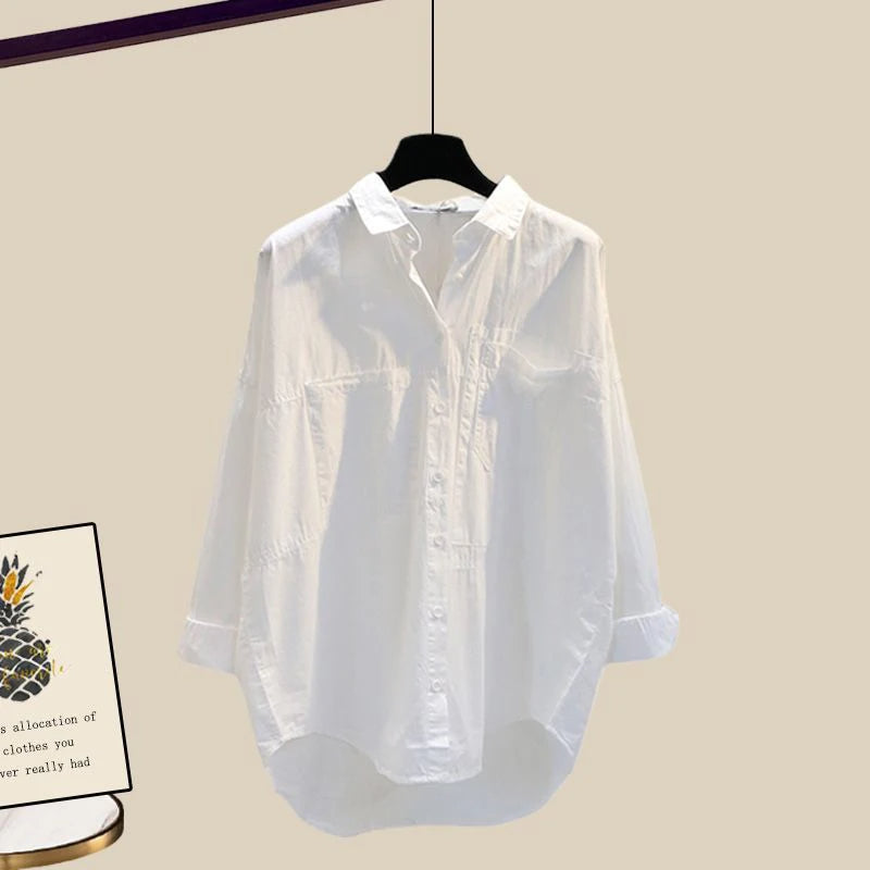 Chemise blanche en coton suspendue sur cintre, manches longues, col classique, style décontracté. Fond beige, affiche avec ananas visible à gauche.