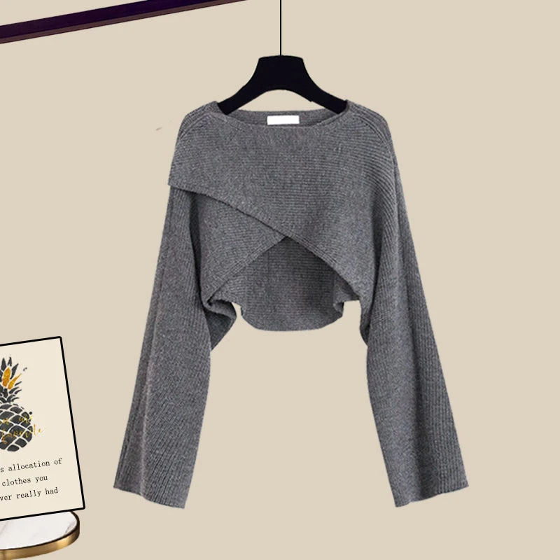 Pull gris en tricot à manches longues, design croisé, suspendu sur un cintre noir. Mode automne-hiver, style décontracté et élégant.