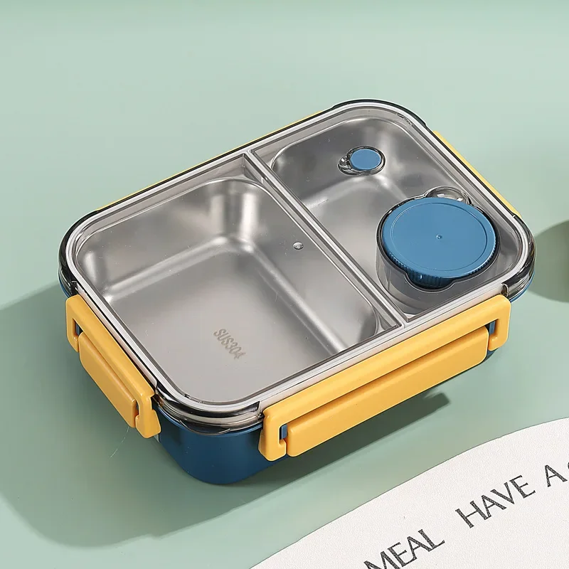 Boîte à lunch en acier inoxydable avec compartiments, couvercle transparent et poignées jaunes, idéale pour repas équilibrés et conservation alimentaire.