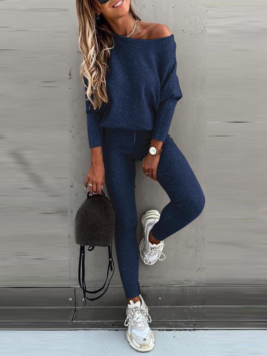 Femme en tenue décontractée bleu marine, portant un pull ample et un legging, avec des baskets blanches et un sac à dos noir. Mode urbaine chic.