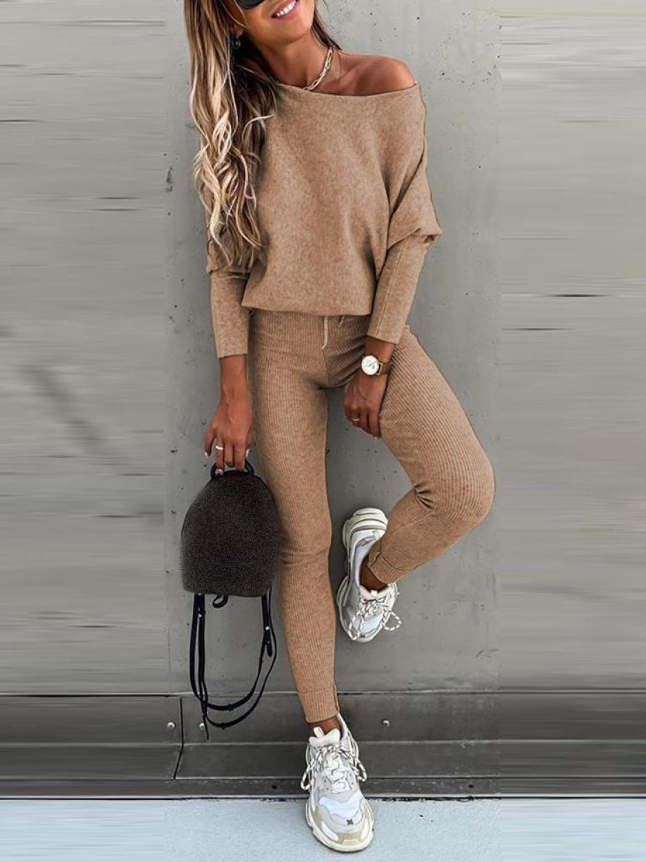 Femme en tenue décontractée beige, pull ample et leggings, portant des baskets blanches et un sac à main noir. Mode automne chic et confortable.