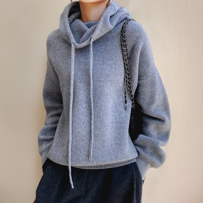 Pull à capuche gris en laine, manches longues, porté par une personne, avec un sac à bandoulière chaîne noire. Mode automne-hiver, style décontracté.