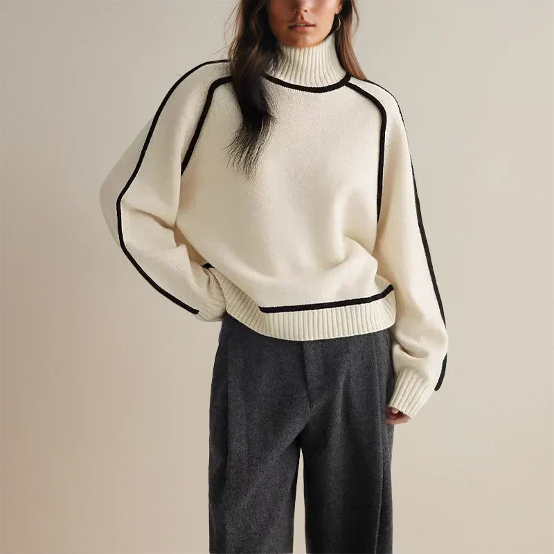 Femme portant un pull blanc à col roulé avec bordures noires et pantalon gris. Mode automne-hiver, style élégant et décontracté.
