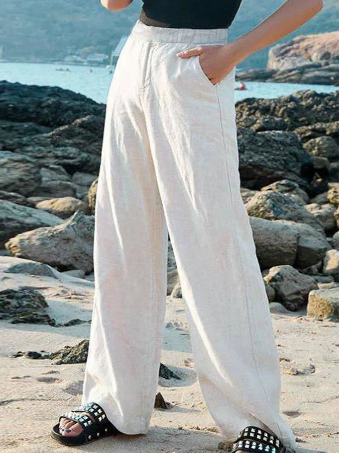 Pantalon large en lin blanc porté sur une plage rocheuse, avec des sandales noires à clous. Mode estivale, tenue décontractée, bord de mer.