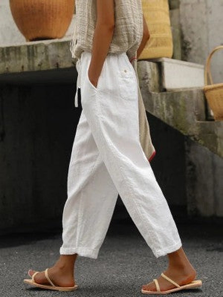 Personne portant un pantalon blanc ample en lin, sandales beiges, et un haut beige texturé. Mode décontractée estivale, style confortable et élégant.