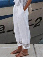 Pantalon blanc en lin avec détails en dentelle, porté par une femme près d'un bateau. Mode estivale, tenue décontractée, style chic et confortable.