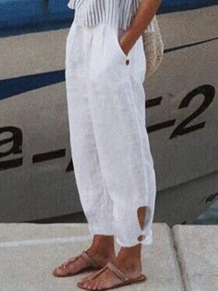 Pantalon blanc en lin pour femme, coupe ample, poches latérales, style décontracté estival, porté avec des sandales marron devant un bateau.