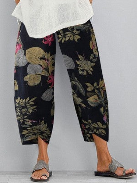 Pantalon ample femme à motifs floraux, fond noir, style décontracté, porté avec sandales tressées. Mode estivale élégante et confortable.