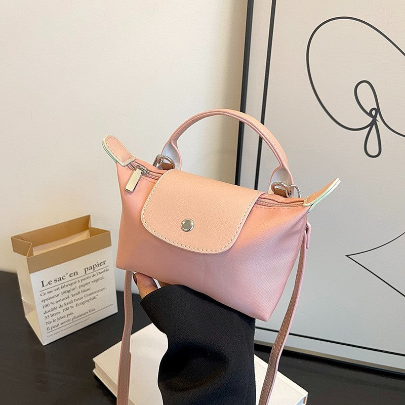 Petit sac à main rose en cuir, design élégant, posé sur une table avec une boîte en papier et une affiche artistique en arrière-plan. Accessoire mode tendance.