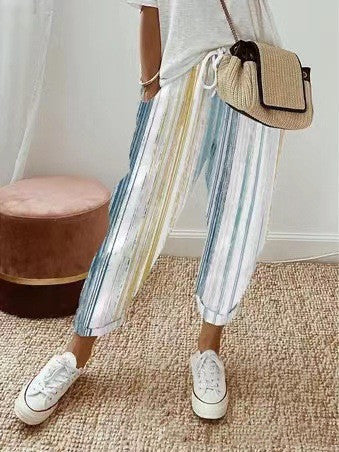 Pantalon rayé multicolore femme, style décontracté, avec t-shirt blanc et sac en osier. Mode estivale, tendance, confortable.