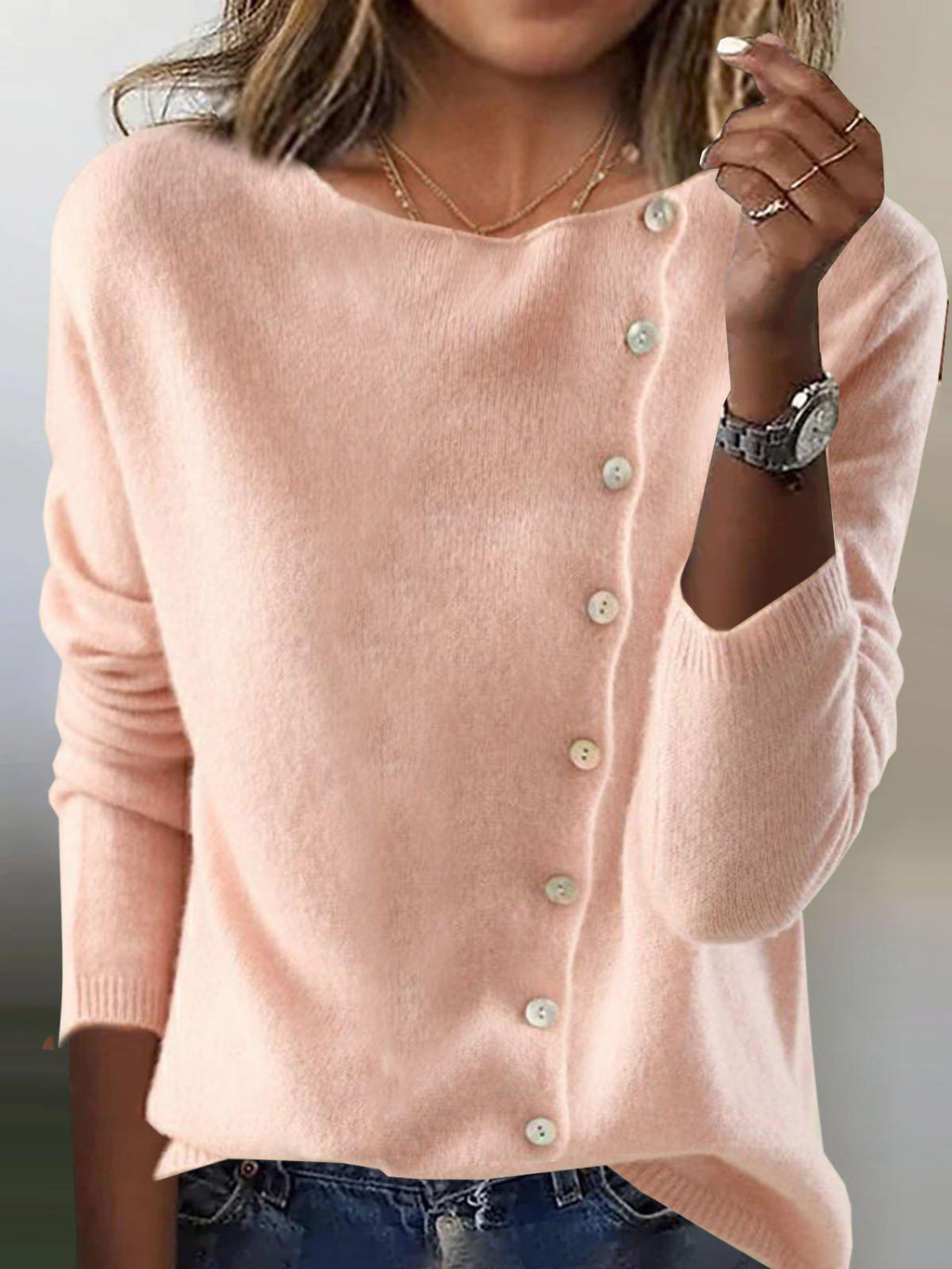 Femme portant un pull rose en laine avec boutons décoratifs, manches longues, col rond, style décontracté. Mode féminine automne-hiver tendance.