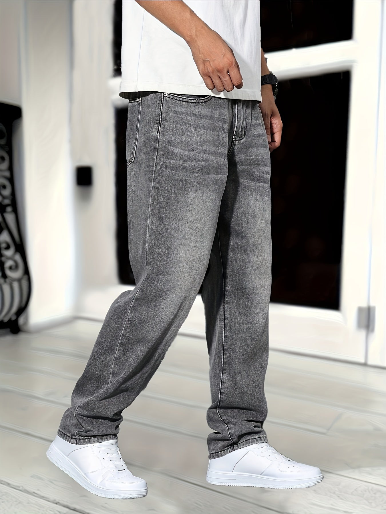 Jeans gris décontractés portés par un homme, associés à des baskets blanches, sur fond de porte moderne. Mode urbaine, style casual, tendance masculine.