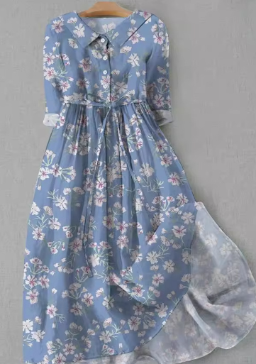 Robe longue bleue à motifs floraux, manches longues, col chemise, ceinture à nouer, style vintage, suspendue sur un cintre en bois.
