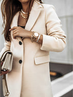 Femme en manteau beige élégant, tenant un sac à main chaîne dorée, montre et bracelets dorés, style chic et moderne, mode automne-hiver.