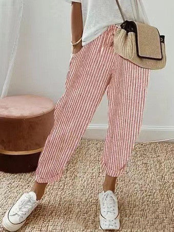 Femme portant un pantalon rayé rouge et blanc, t-shirt blanc, baskets blanches, sac en osier. Mode décontractée, tendance estivale, style chic.