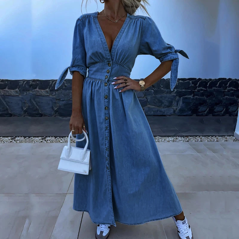 Robe en jean bleu à manches courtes avec boutons, portée par une femme tenant un petit sac blanc. Mode décontractée, tendance et élégante.