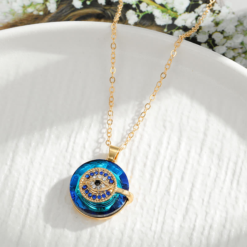 Collier pendentif en or avec pierre bleue et motif circulaire incrusté de cristaux, posé sur une assiette blanche. Bijoux élégants et modernes.