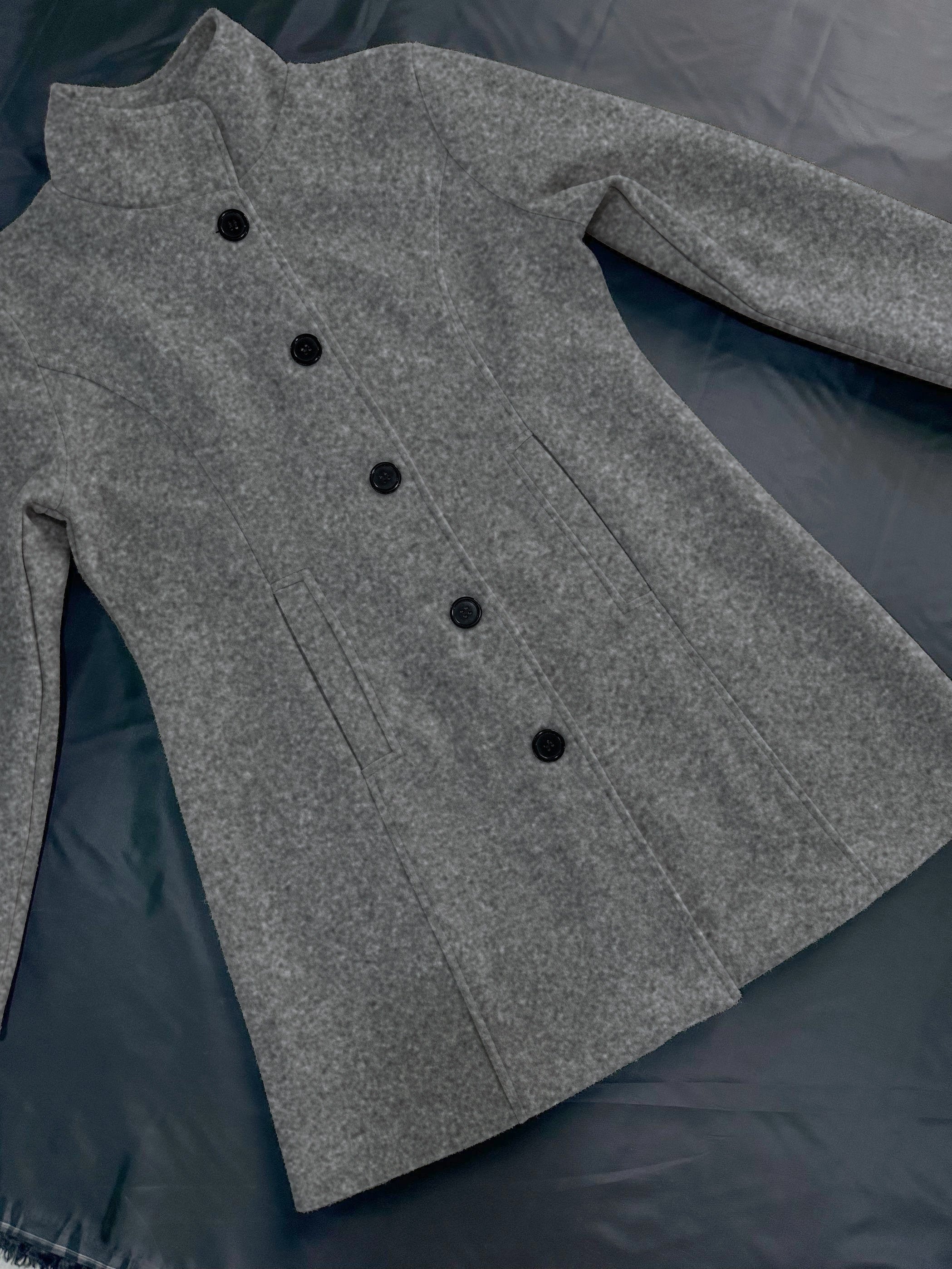 Manteau gris en laine pour femme, élégant et chaud, avec col montant et boutons noirs, posé sur une surface sombre. Mode hiver tendance.