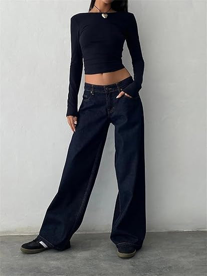 Femme portant un haut noir ajusté et un jean large bleu foncé, posant contre un mur blanc. Mode décontractée, tendance streetwear.
