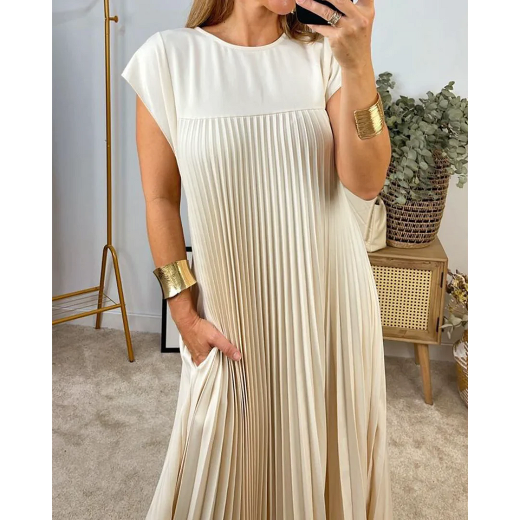 Robe plissée beige élégante portée par une femme, avec bracelets dorés, dans un intérieur moderne. Mode féminine, style chic, tenue tendance.