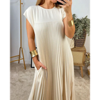 Robe plissée beige élégante portée par une femme, avec bracelets dorés, dans un intérieur moderne. Mode féminine, style chic, tenue tendance.