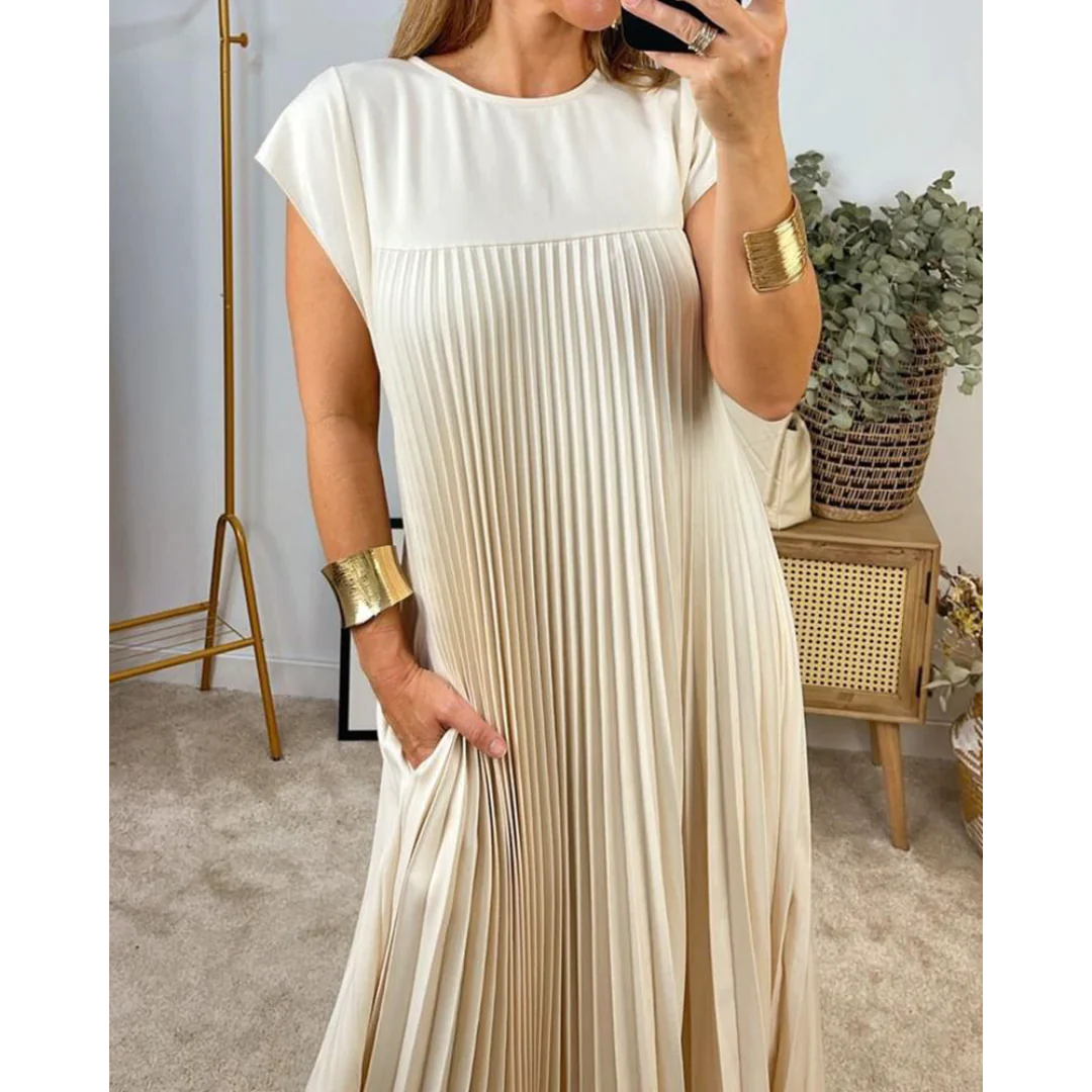 Robe plissée beige élégante portée par une femme, avec bracelets dorés, dans un intérieur moderne. Mode féminine, style chic, tenue tendance.