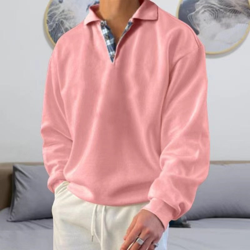 Homme portant un pull rose à col polo, chemise à carreaux en dessous, pantalon blanc. Style décontracté, mode masculine, intérieur moderne.
